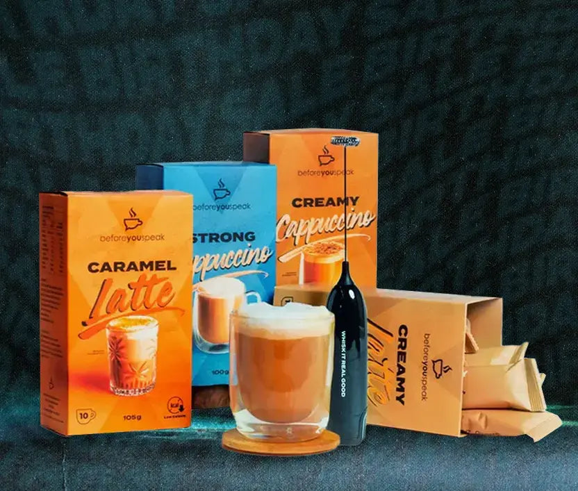 A coffee mix product display featuring several colorful boxes of coffee creamer and milk powder, a dark bottle, and a prepared cappuccino in a glass on a dark textured background.